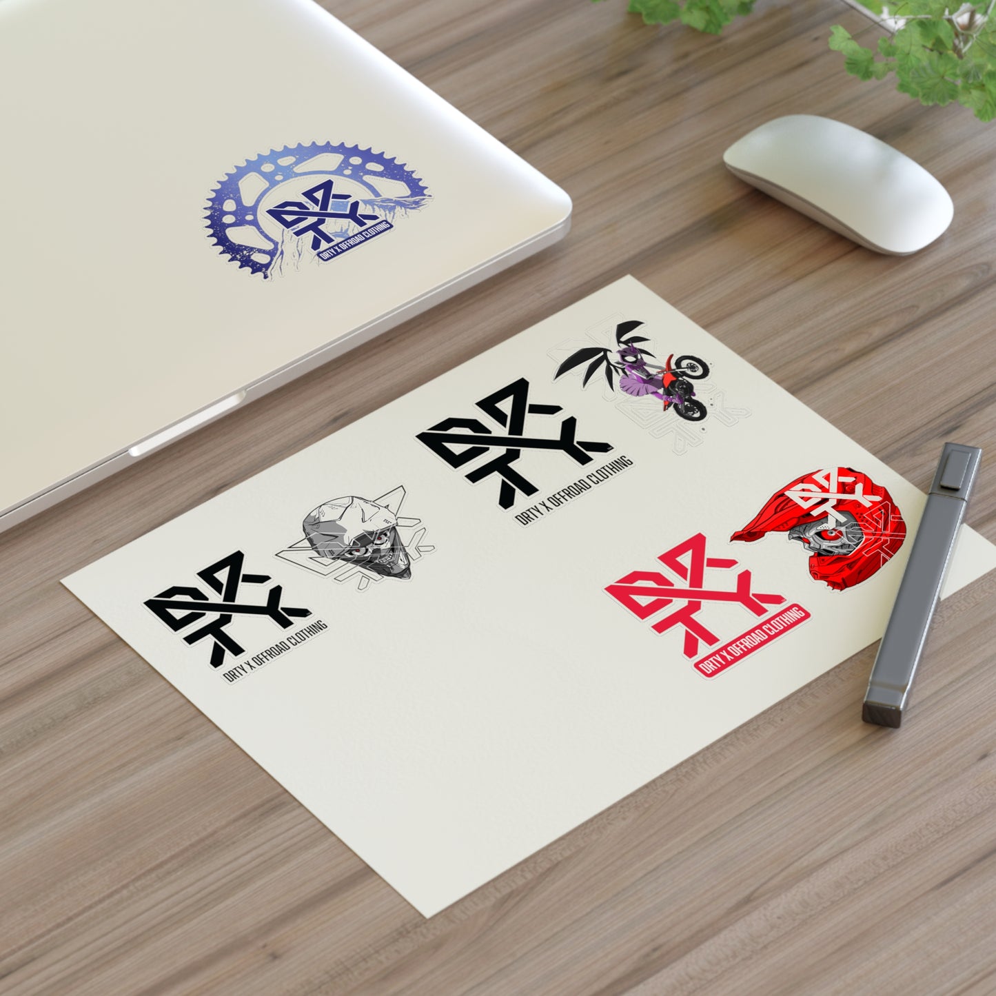 This image shows a small DRTY X logo and artwork sticker on a laptop background and sticker sheet on a table