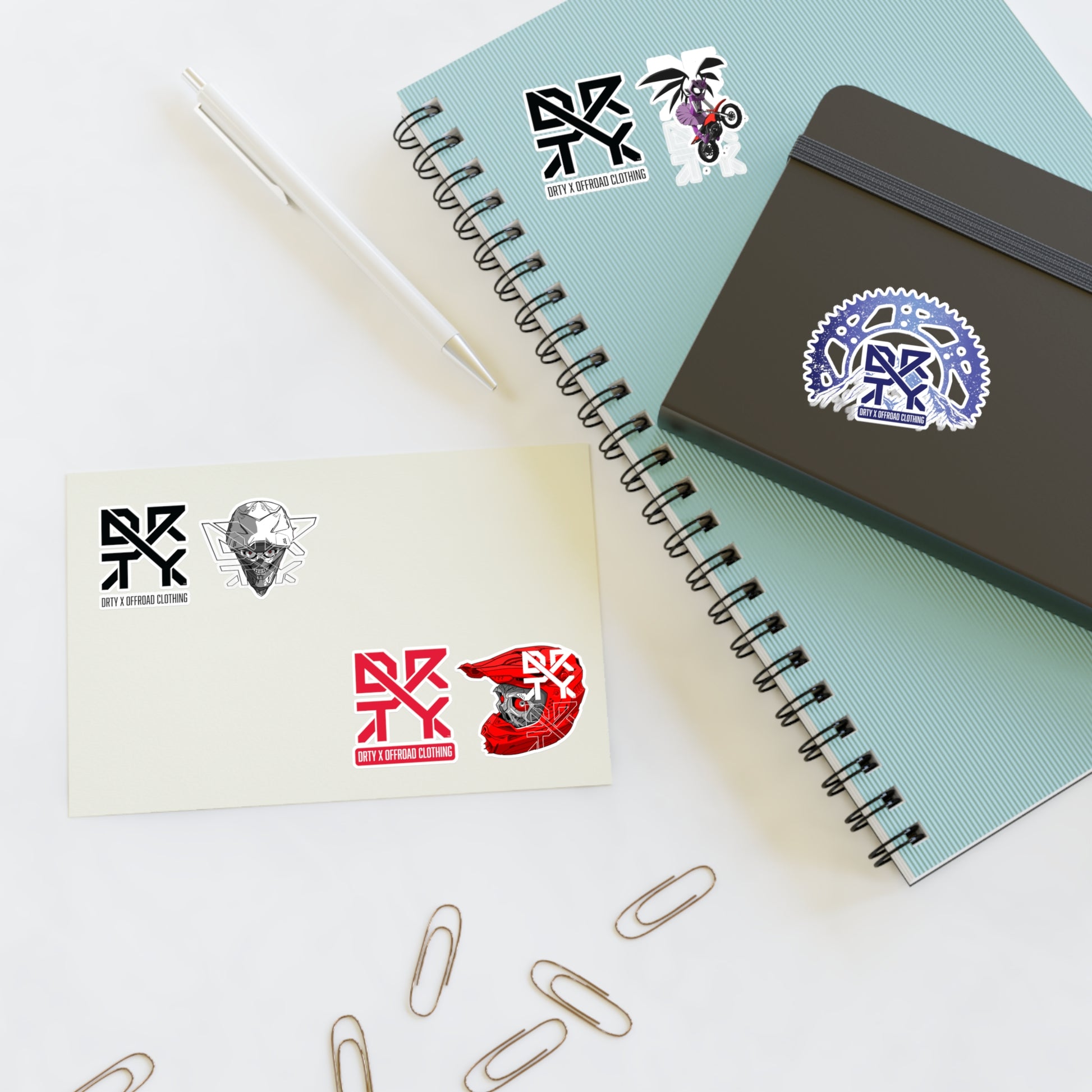 This image shows a small DRTY X Logo and artwork sticker on a notepad,and sticker sheet on a table.