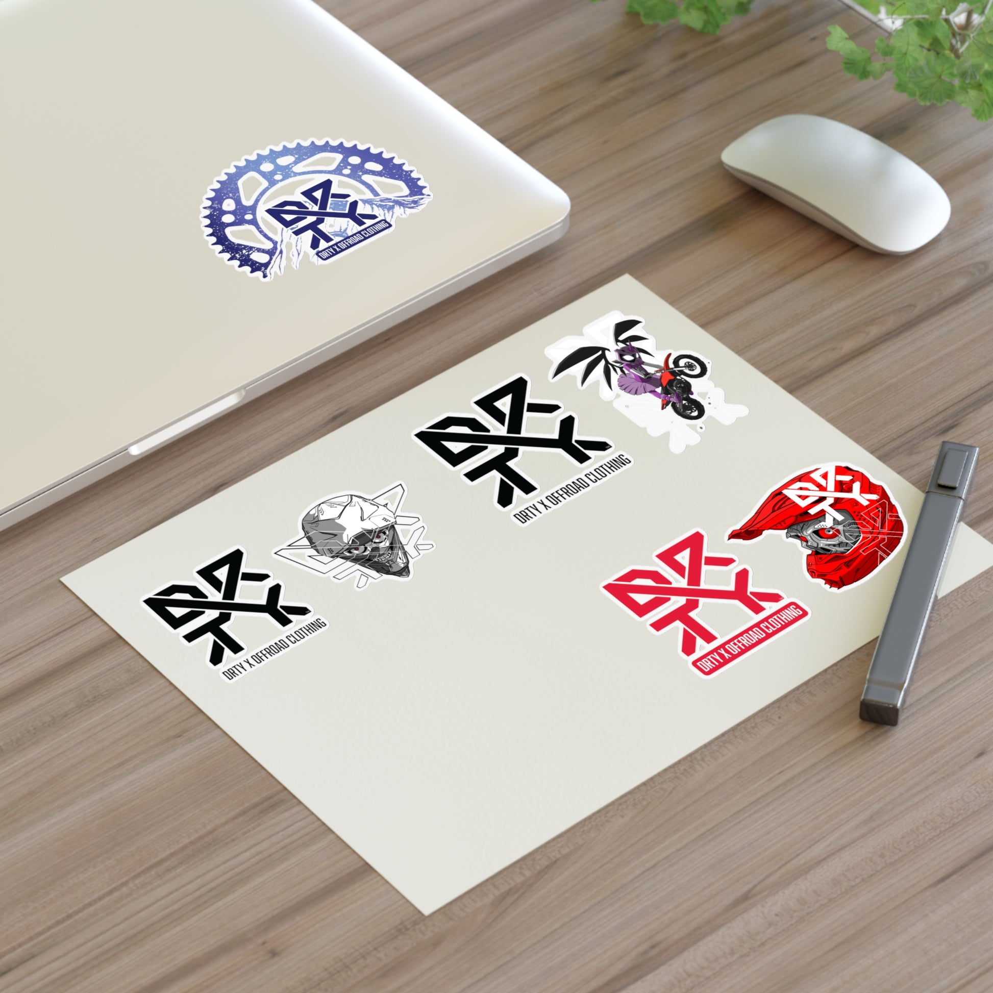 This image shows a small DRTY X logo and artwork sticker on a laptop background and sticker sheet on a table