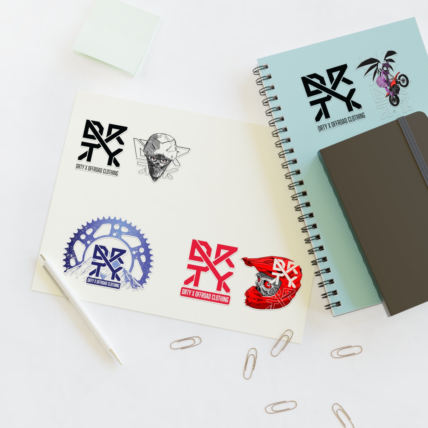 This image shows a small DRTY X Logo and artwork sticker on a notepad,and sticker sheet on a table.