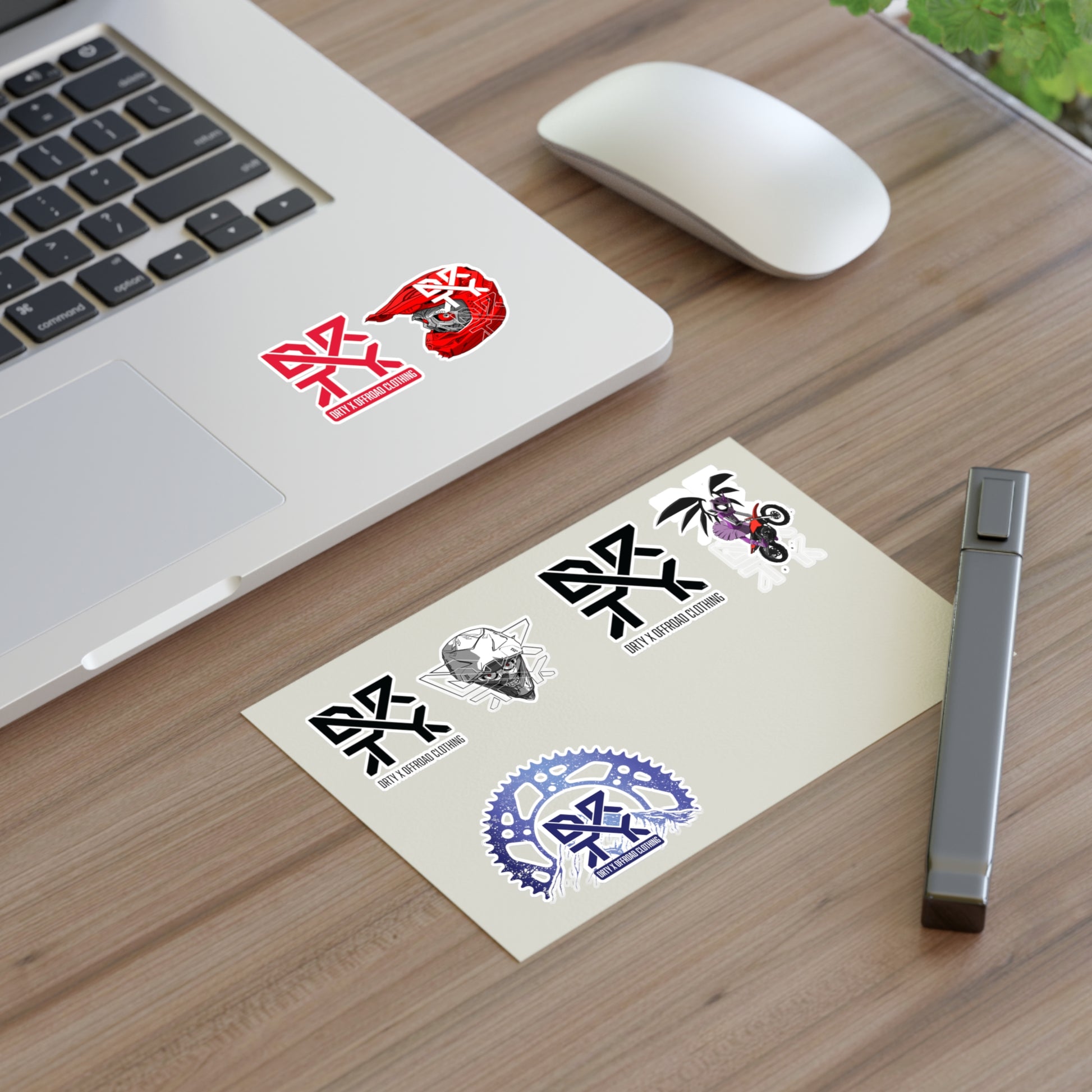 This image shows a small DRTY X logo and artwork sticker on a laptop background and sticker sheet on a table