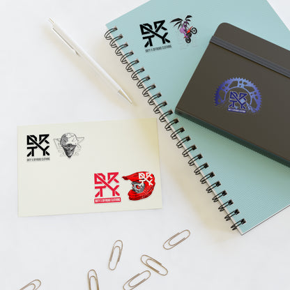 This image shows a small DRTY X Logo and artwork sticker on a notepad, and sticker sheet on a table